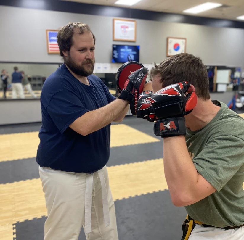 Adult martial arts participants kicking pads during stress-relief workout session